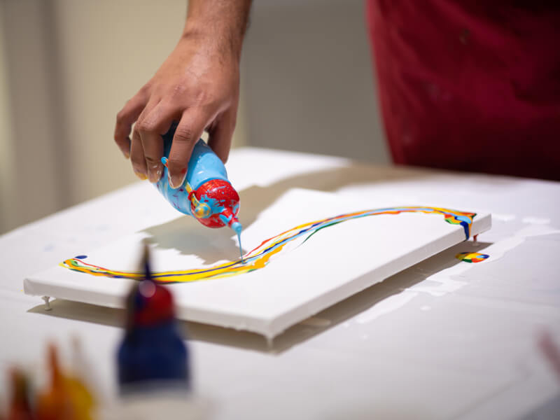 A close up of a person pouring coloured paint onto a canvas from a bottle