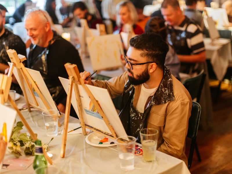 Man painting on a canvas in a paint and sip class