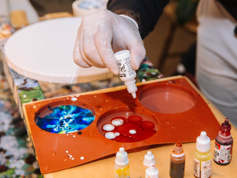 A close up of a person mixing paint colours ready for a paint pouring class
