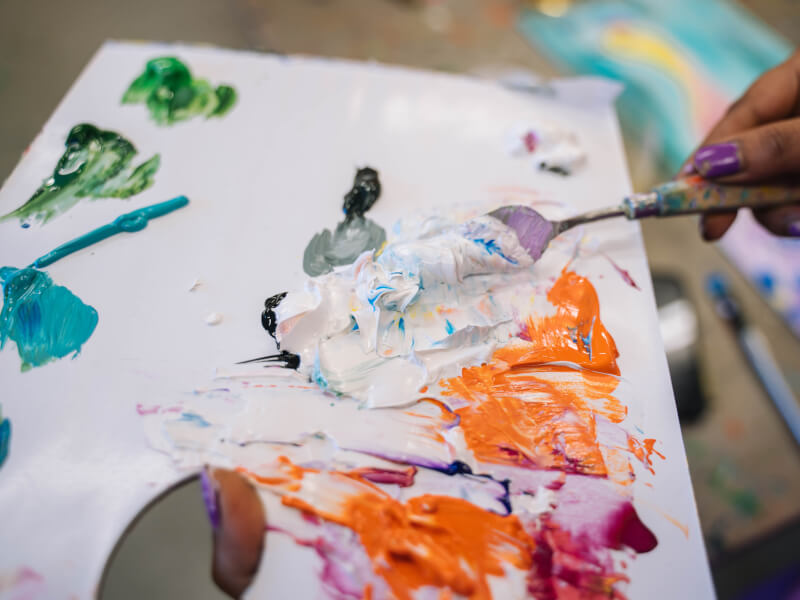 A close up of a person mixing paint colours using a pallette knife