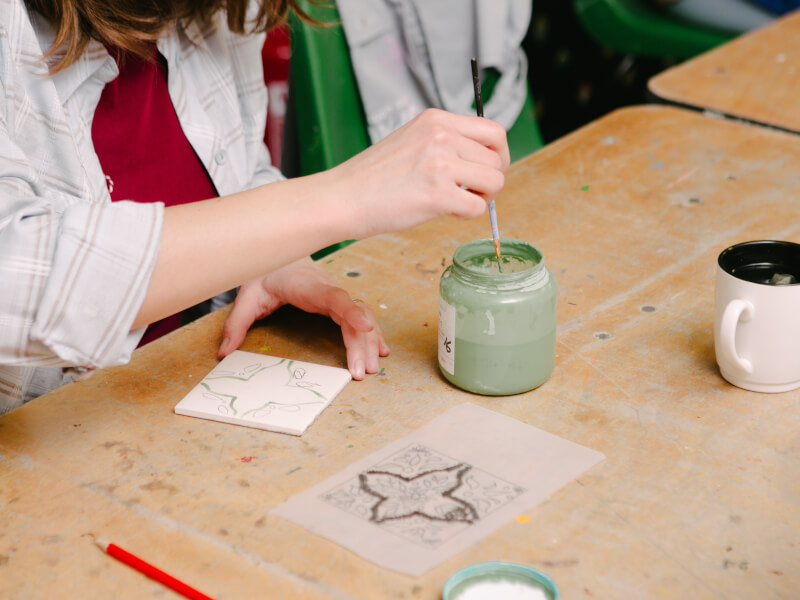 A close up of a person painting a green design on a white tile