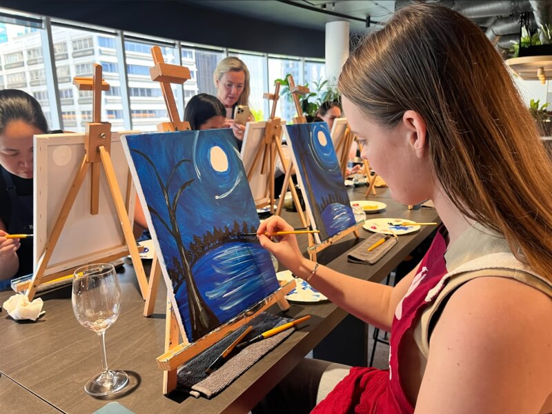 Woman painting a nighttime landscape in a paint and sip class