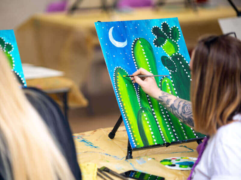 Someone painting cacti on a canvas in a painting class