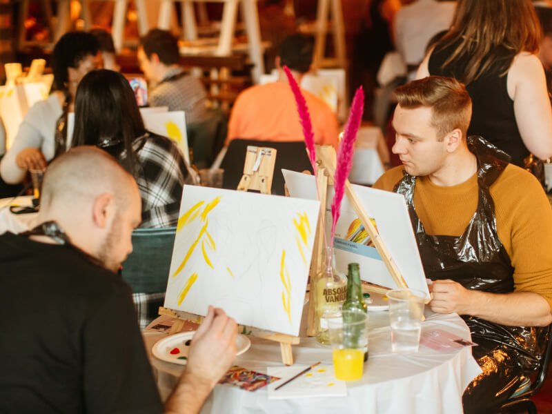 Two men add paint to their canvas at a sip and paint event.
