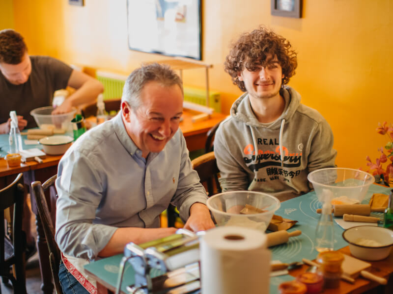 Two men smiling with pasta-making ingredients in a cooking class.
