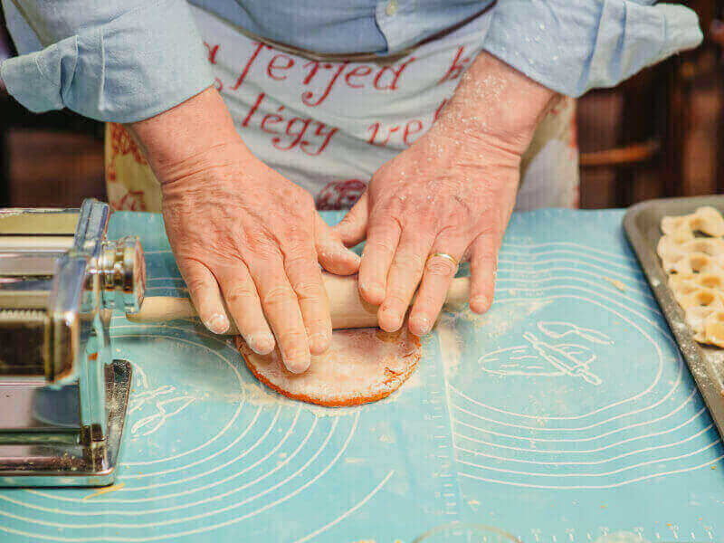 Hands using a rolling pin to roll pasta dough. 