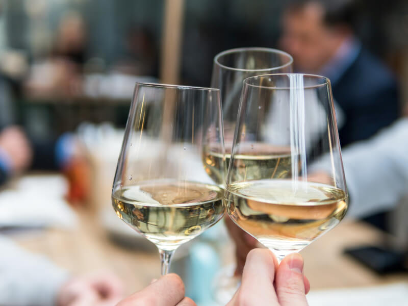 Three people are clinking glasses of white wine together in a 'cheers' style
