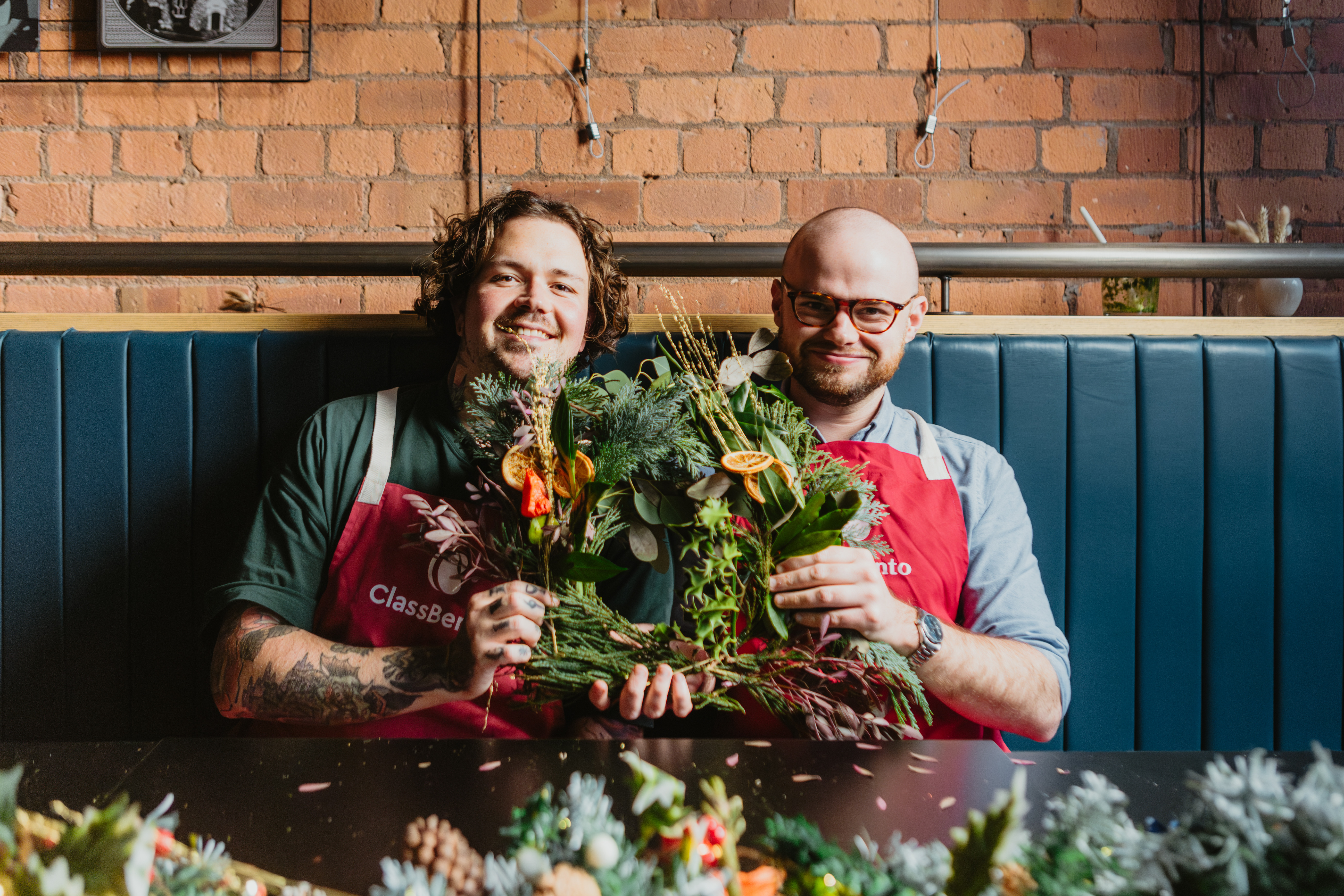 Two smiling people holding a handmade Christmas wreath