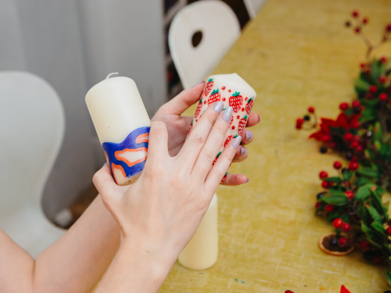 A close up of a person holding two candles, decorated with hand painted strawberries and a colourful swirl pattern