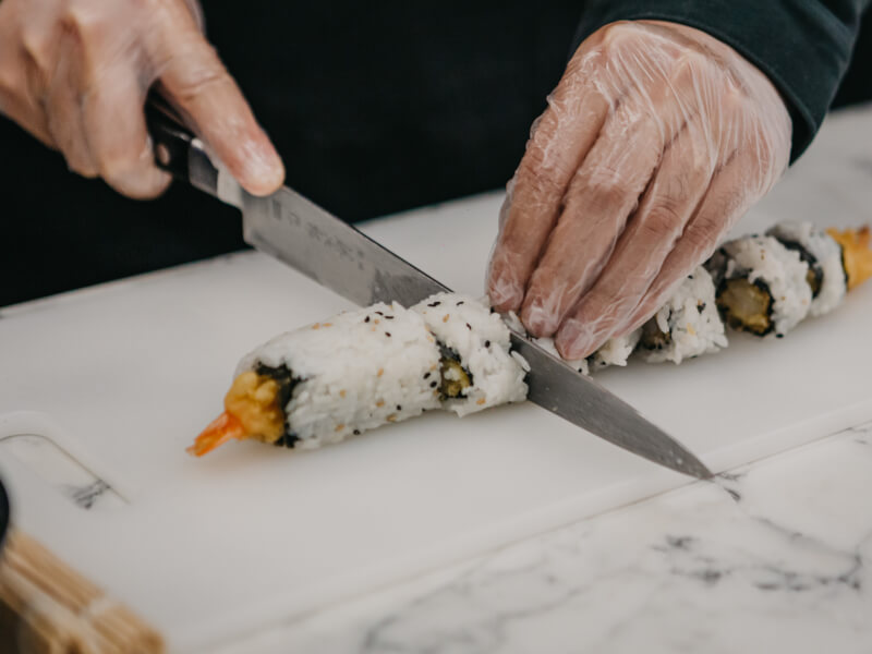 A close up of a person cutting sushi into pieces