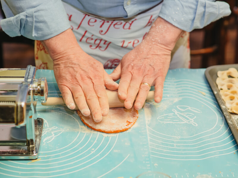 A close up of a person rolling out orange pasta dough 