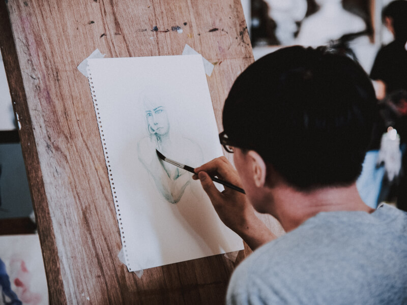 Man painting a drawing on an easel at an art class.
