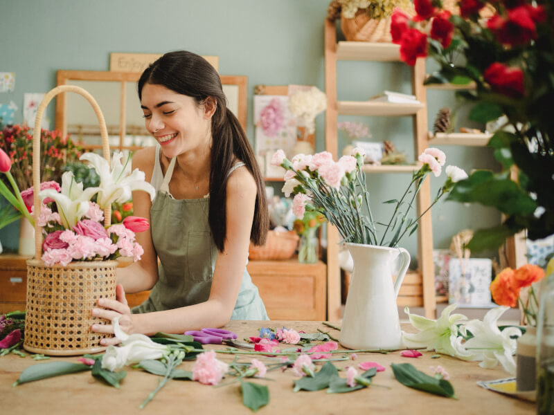 A person working at a cluttered table as they make floral arrangements