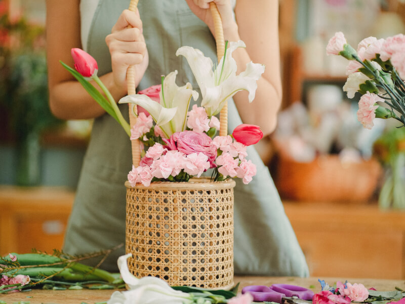 A person is holding a flower arrangement in a wicker basket