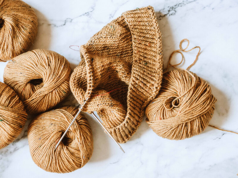 Five balls of mustard yarn sit on a marble table with some half-finished knitting