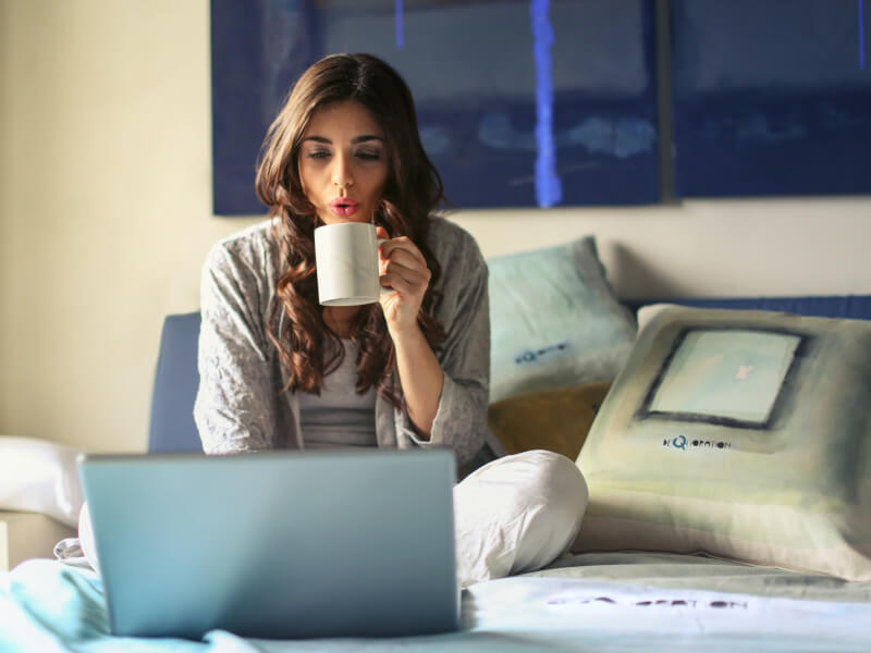 A person drinking a hot drink whilst on a laptop