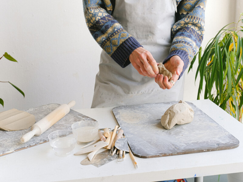 A person standing at a table covered in clay and tools, moulding a piece of clay