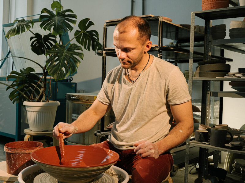 A person sits at a pottery wheel, adding colour to a handmade pottery bowl