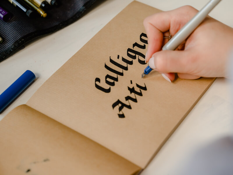 A calligraphy pen writing the word calligraphy on brown paper.