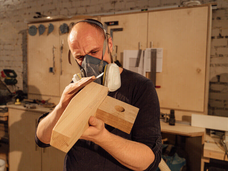 A man hand sands a wooden joint in a woodworking course.