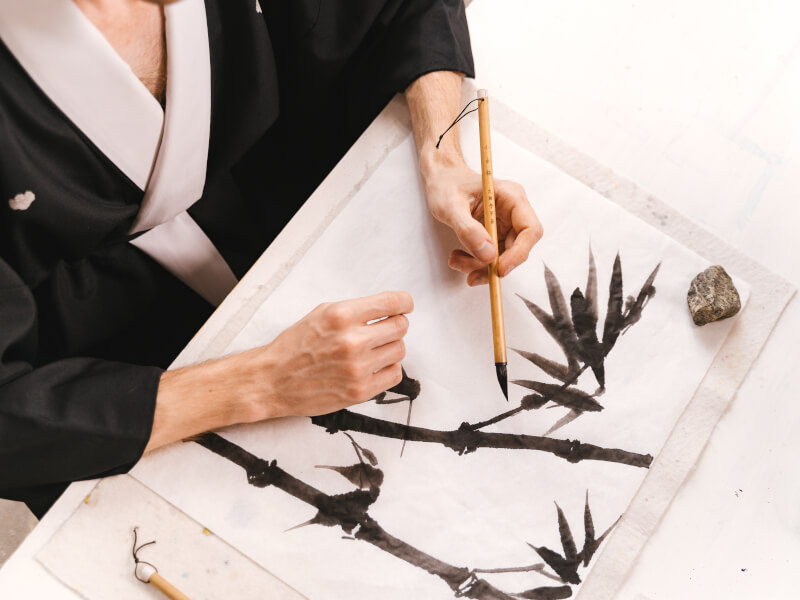 Person in a kimono painting a Japanese-style painting.