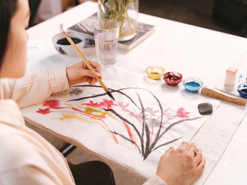 A woman painting colourful flowers on paper.
