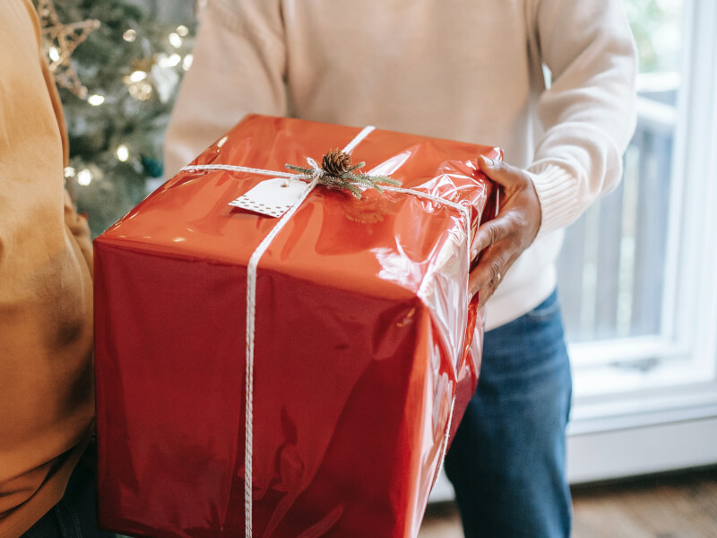 A person handing a wrapped chirstmas present to another person