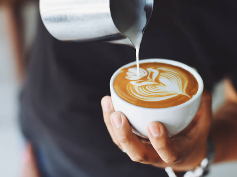 Person pouring milk into coffee and making latte art. 