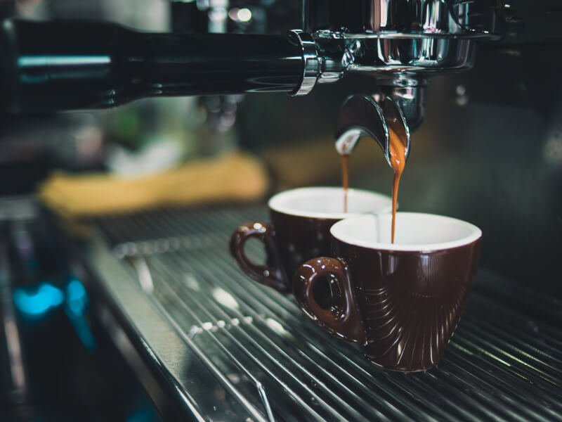 A barista coffee machine dispensing two cups of espresso.