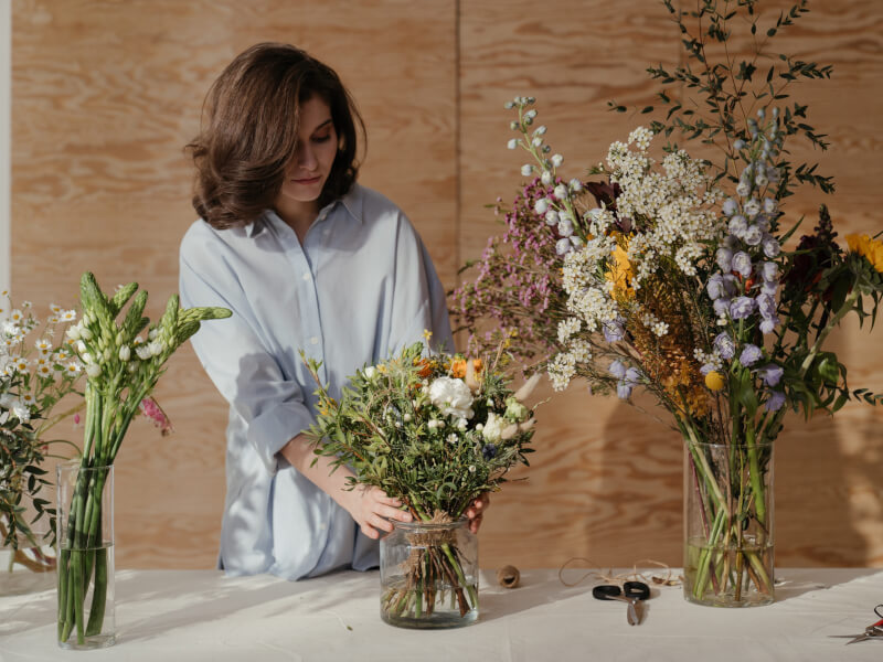 A person in a blue shirt creating floristry arrangements at a floristry class.