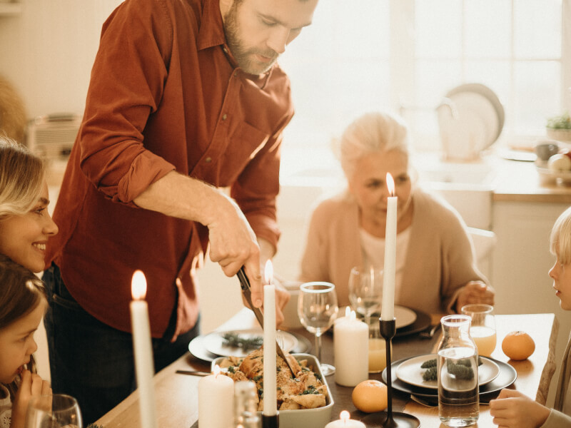A family sitting at a table as the father prepares the meat