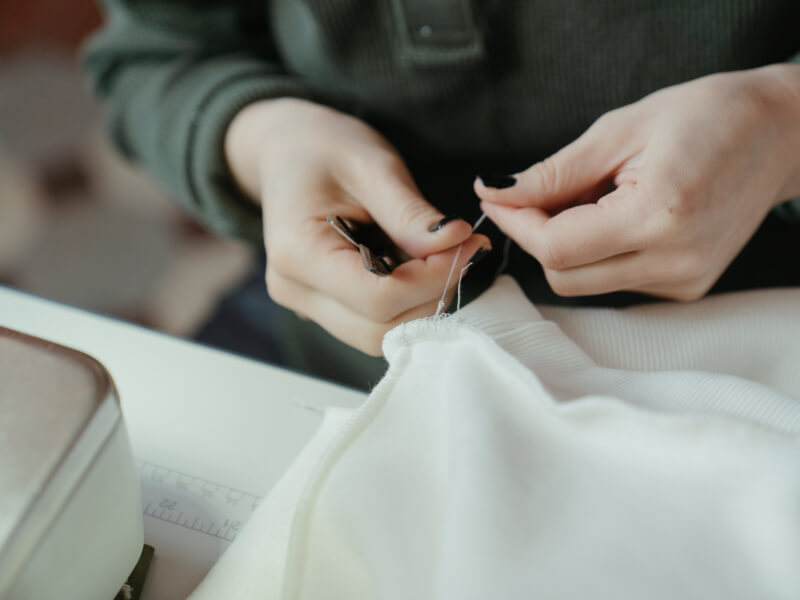 Woman wearing green jumper sewing with an embroidery kit. 