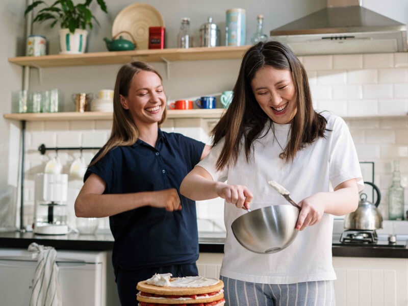 Two people laughing and decorating a sponge cake