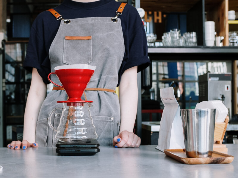 Person wearing an apron stood behind a v60 coffee set up. 