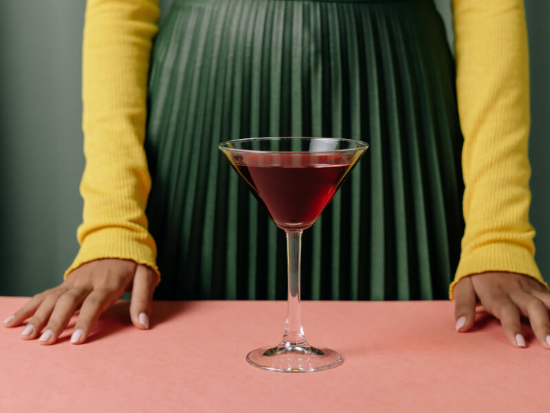 A delicious cocktail placed on a table as a person stands behind it