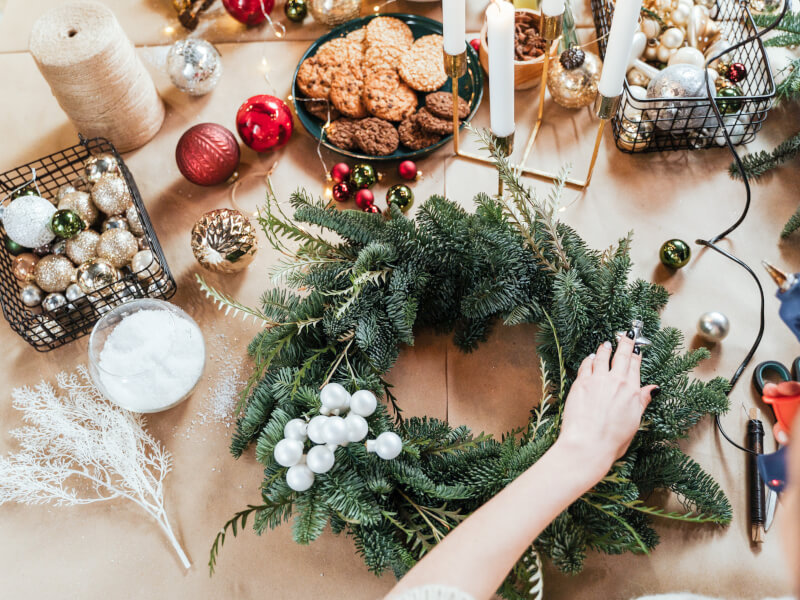 A person is adding baubles to a Christmas wreath
