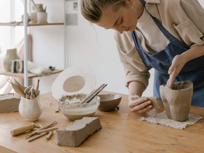 Woman wearing apron making pottery at home with a potter making kit.