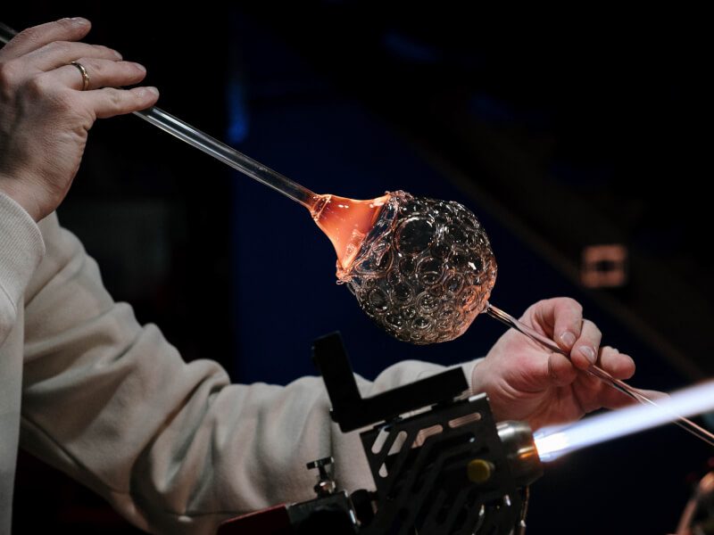 A person is using heat and tools to blow glass