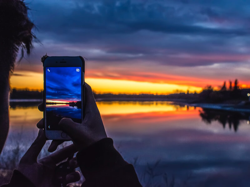 A person taking a photo of a sunset with phone camera.