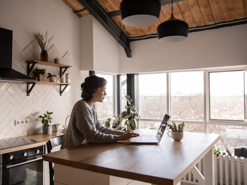 A person sits at a kitchen table whilst busy on their laptop