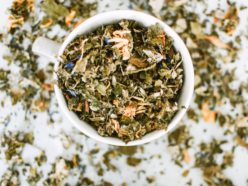 Taken from above, the image shows a white cup on a table, overflowing with loose leaf tea