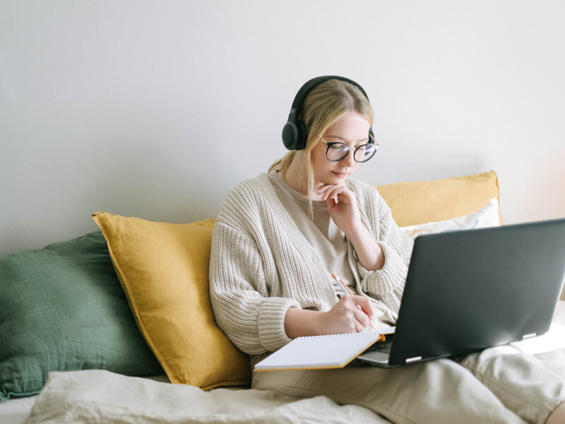 A person concentrating with a laptop and notepad resting on their legs