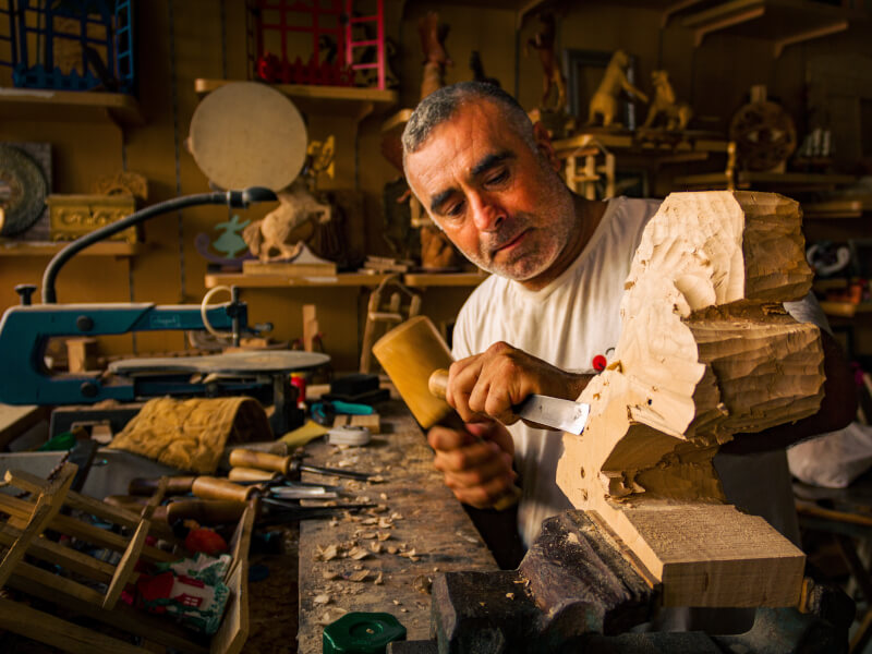 A man is carving some wood art using a chisel in a woodworking workshop