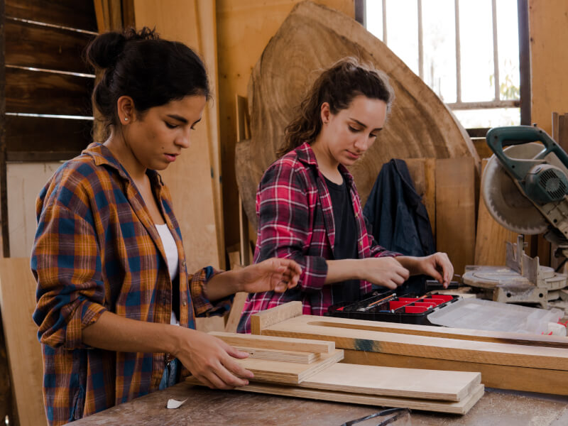 Two women work on their beginner woodworking projects at a class.