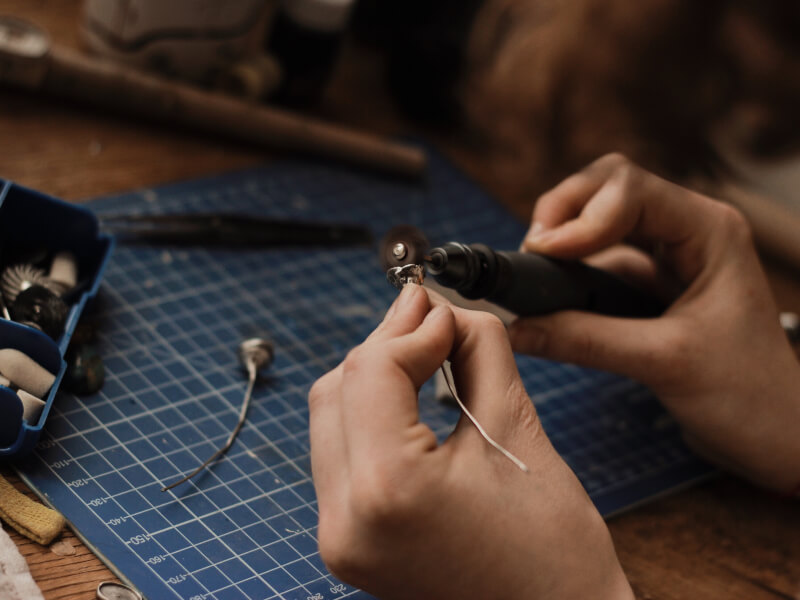 Polishing homemade jewellery using jewellery tool supplies. A blue cutting mat protects the table.