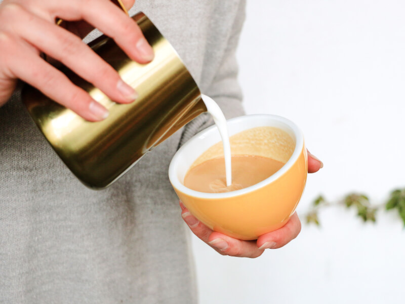 A close up of a person pouring milk into a yellow coffee cup