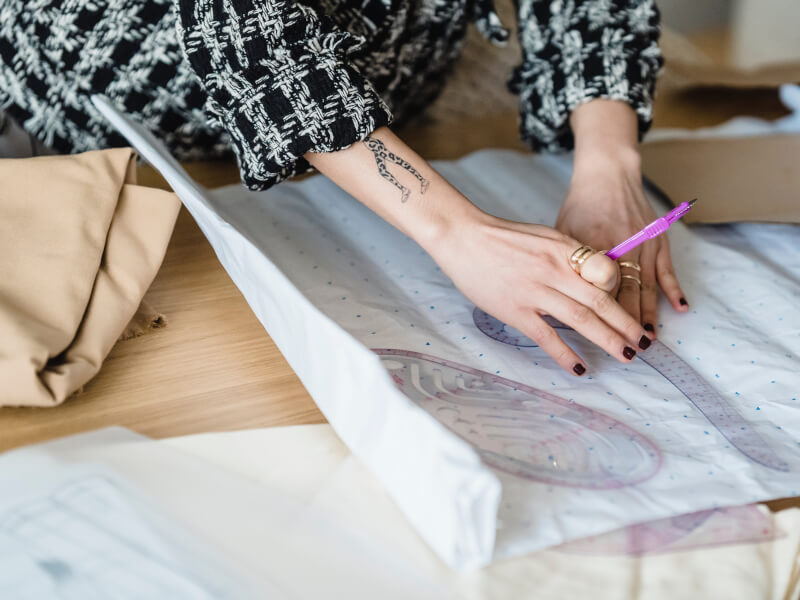 A person is working out a sewing pattern on a piece of grid paper using a plastic tool