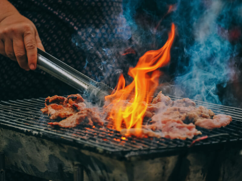 A person using a spatula to flip meat that is cooking on a grill barbecue.