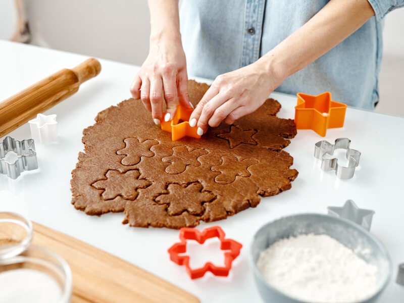 A person is cutting gingerbread men shapes out of a rolled out piece of gingerbread
