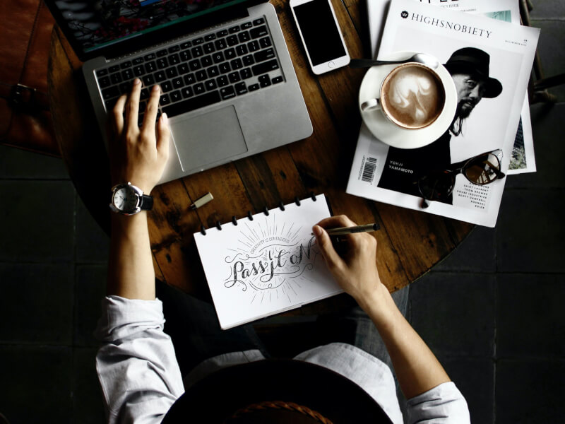 A person sits at their desk as they write using calligraphy lettering